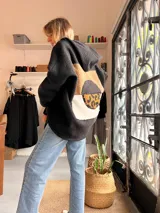 Campera tipo hoodie de textura tipo corderito en color negro, con diseño de collage en la espalda que combina parches en tonos marrón, blanco y estampado animal print de leopardo.