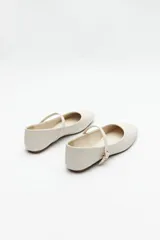 Balerinas color crudo de símil cuero texturizado, con punta redondeada, tira sobre el empeine y hebilla metálica ajustable.