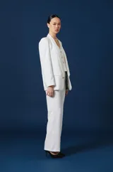 Saco de mujer color bordó con solapas redondeadas, cierre frontal de un botón dorado y bolsillos laterales con solapa. Presenta un parche decorativo en la manga izquierda y un broche metálico en la solapa.