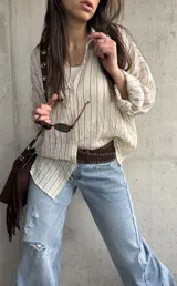 Camisa beige de rayas verticales, de calce relajado y tejido liviano, con mangas largas y cuello camisero.