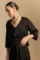 Blusa negra de satén con escote en V y detalle de volados frontales. Presenta mangas largas con puños abotonados y una silueta fluida.