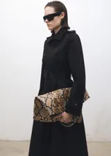 Trench coat largo de color negro con diseño de doble botonadura, cuello con solapa, trabillas en hombros y puños, y cinturón desmontable con hebilla. Cuenta con forro interior y abertura posterior.