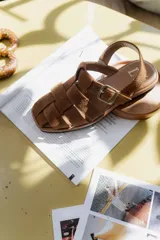 Sandalias marrones de cuero con diseño de tiras entretejidas y hebilla lateral.