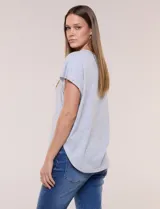 Remera de silueta amplia y relajada de color gris melange, confeccionada en algodón con poliéster. Presenta escote a la base con terminación rústica de borde enrollado, mangas cortas de hombro caído sin dobladillo y ruedo curvo con la parte posterior más larga.