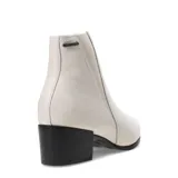 Bota de caña baja marca Bottero, confeccionada en cuero color marfil. Presenta un diseño minimalista con panel elástico lateral, punta redondeada y taco cuadrado en contraste de color negro.