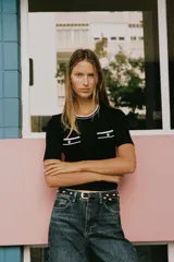 Camiseta negra de manga corta y corte slim fit, con cuello redondo ribeteado en blanco y dos bolsillos de plastrón en el pecho con un botón dorado cada uno.
