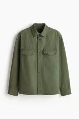 Camisa cargo color verde militar de corte regular, confeccionada en tejido ripstop de algodón. Cuenta con cuello inglés, cierre frontal de botones, bolsillos con solapa en el pecho y mangas largas con puños abotonados.