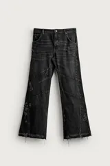 Jeans flare fit de denim de algodón negro con efecto desgastado, roturas, costuras decorativas en las perneras y bajo irregular deshilachado.