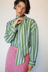 Camisa de rayas rojas y celestes, con cuello subido y lazada en el mismo tejido, manga larga con puños y bajo asimétrico.