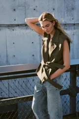 Chaleco de cuello solapa y escote pico cruzado, con hombreras y manga sisa. Presenta bolsillos de vivo en el delantero, forro interior y cierre frontal cruzado con botones. Incluye un cinturón de lazada en el mismo tejido.