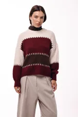 Sweater de tejido de punto grueso con diseño de bloques de color en tonos beige, marrón y bordó. Presenta un corte relajado, mangas amplias y detalles de costuras visibles en contraste que separan las franjas de color.