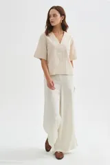 Blusa de viscosa color beige con cuello en V, mangas cortas amplias y detalles de pespuntes decorativos en el frente y las mangas.