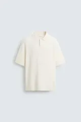 Polo de manga corta color crema, tejido en punto, con cuello solapa y cierre frontal de dos botones. Presenta un calce regular y acabados en rib.