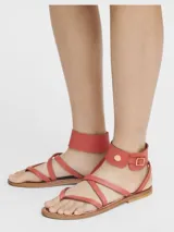 Sandalias planas de cuero color rojo, diseñadas en colaboración entre Longchamp y K. Jacques. Presentan un diseño de tiras finas cruzadas sobre el empeine y una tira ancha envolvente en el tobillo con cierre de hebilla dorada y detalle de botón metálico. La suela es plana de cuero en tono natural.