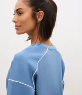 Buzo deportivo Get Over oversized de modal en color celeste, con cuello redondo, manga larga y detalles de costuras y frisos en color blanco.