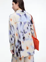 Camisa oversized de manga larga confeccionada en viscosa crinkled con estampado de manchas en tonos blanco, negro y marrón. Presenta bolsillos frontales grandes, tajos laterales y un largo extendido en la espalda.