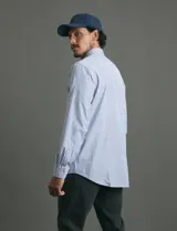 Camisa de manga larga con estampado de rayas verticales en azul y blanco, cuello clásico y bolsillo frontal.