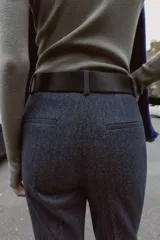 Pantalón de tiro alto con diseño de espiga, corte recto y nervio marcado en el frente. Incluye un cinturón ancho con hebilla metálica dorada y cierre lateral con cremallera oculta.