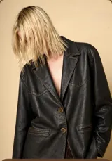 Blazer de cuero vacuno en color negro con efecto gastado y costuras a la vista. Presenta solapas clásicas, cierre frontal con dos botones y bolsillos laterales con solapa.