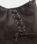 Cartera estilo hobo de cuero sintético en color gris oscuro, con diseño de media luna y correa fija para el hombro. Cuenta con bolsillos frontales funcionales, detalles de ojalillos metálicos plateados y un cordón cruzado ajustable con lazo en el centro.