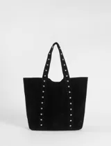Cartera tipo shopper de gran tamaño confeccionada en material efecto gamuza color rojo. Presenta correas reforzadas decoradas con tachas metálicas plateadas y un dije colgante en forma de corazón con detalles de tachas. Cuenta con una placa metálica pequeña con logo en la parte inferior frontal.