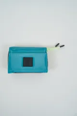 Billetera plegable color naranja con cierre de velcro y detalle de cordón marrón en el lateral. Presenta un parche negro con texto en relieve en la solapa frontal.