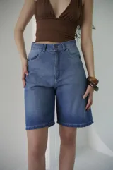 Bermuda de denim azul claro, de tiro medio y largo a la rodilla, con calce relajado y silueta amplia. Cuenta con bolsillos delanteros y traseros, y cierre frontal con botón y cremallera.