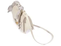 Mini bolso de mano Schutz modelo Brera, color blanco con textura granulada, solapa frontal con cierre metálico dorado y plateado, asa superior decorada con pañuelo estampado y correa ajustable para llevar al hombro o cruzado.