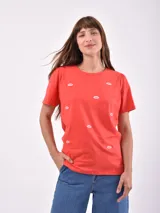 Remera de algodón color rojo con cuello redondo, mangas cortas con sutil frunce en los hombros y estampado de labios blancos dispersos por toda la prenda.