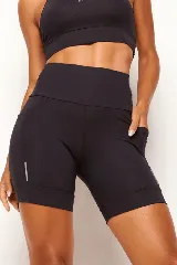 Short tipo biker de compresión moderada, color negro, con cintura alta anatómica que incluye bolsillo interno 360° y bolsillos laterales funcionales. Presenta detalles reflectivos en los laterales y dobladillo reforzado.
