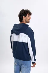 Canguro deportivo de color azul marino con un bloque horizontal blanco en contraste sobre el pecho y las mangas. Posee capucha y puños elásticos.
