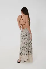 Vestido largo de crochet color crudo con motivo de medallones y forro interior negro. Cuenta con escote en V, espalda descubierta y tirantes de cuero marrón.