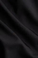 Top negro de punto elástico con escote asimétrico de un hombro, detalle de metal plateado y tira larga. Diseño entallado con laterales fruncidos para crear un efecto drapeado.