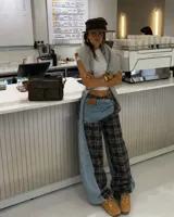 Pantalón de corte ancho y tiro bajo, confeccionado con un diseño híbrido de denim celeste y tela a cuadros en tonos azul marino y amarillo. Presenta detalles de superposición y cierre decorativo en la parte frontal.