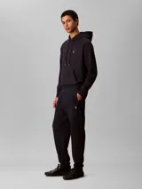 Pantalón de jogging Calvin Klein de felpa color azul marino, con cintura elástica, cordón ajustable, bolsillos laterales y puños elásticos en los tobillos. Cuenta con el monograma CK bordado discretamente en la pierna.