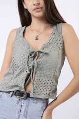 Chaleco corto sin mangas color verde salvia, confeccionado en tela perforada (broderie o calado). Presenta escote en V con lazos ajustables en el centro frontal.