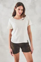 Remera color crudo de algodón peinado, de corte recto y mangas cortas. Presenta cuello redondo con detalle de cadena metálica dorada.