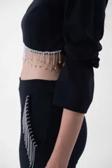 Top negro corto con mangas largas, cuello redondo y detalle de flecos de strass colgantes en el ruedo.