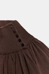 Blusa marrón de punto fluido, con cuello subido abotonado en un lateral y mangas largas con puños ajustados. Presenta un diseño fruncido en la parte frontal que aporta volumen.