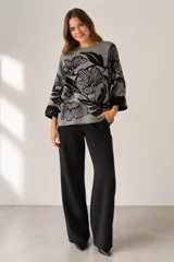 Buzo de punto de corte holgado con diseño estampado floral en tonos gris y negro. Presenta cuello redondo, mangas tres cuartos con puños acentuados y una textura suave.