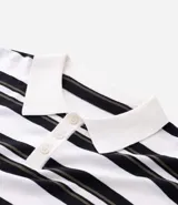 Remera boxy de punto listrado en blanco, negro y verde oliva, con cuello polo y abertura frontal con botones. Posee caída cómoda y textura suave.