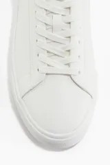 Championes blancos de cuero sintético con suela plana y cordones. Diseño minimalista.