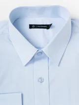 Camisa de vestir de manga larga, color blanco, con cuello clásico y cierre frontal de botones. Presenta un corte slim fit y una textura sutilmente rayada en la tela.