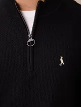 Sweater de punto color negro, con cuello alto y cierre frontal parcial tipo medio cierre. Presenta textura en el tejido y logo bordado en el pecho.