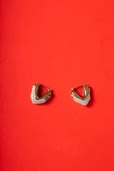 Aros tipo argolla de diseño escultórico y asimétrico, combinando metal dorado con resina en tono marmolado claro.