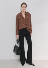 Camisa de poliéster color marrón con estampado de lunares blancos, cuello camisero, manga larga y cierre frontal de botones ocultos.