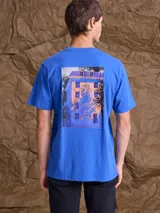 Remera de manga corta color azul con estampa artística en la espalda que representa una fachada de edificio con sombras.