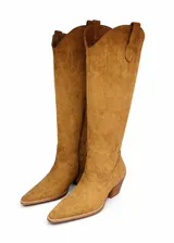 Botas texanas de caña alta confeccionadas en gamuza color camel, con diseño de costuras decorativas en la caña, punta fina y taco cuadrado de madera.