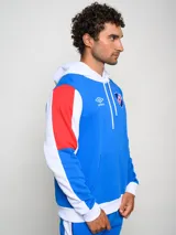 Canguro de felpa Umbro del Club Nacional de Football, con diseño tricolor en rojo, azul y blanco. Presenta capucha con cordones ajustables, bolsillo tipo canguro frontal, logo de la marca y escudo del club bordados en el pecho.