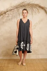 Vestido negro con escote en V, corte holgado, largo midi y volado bordado en el ruedo.